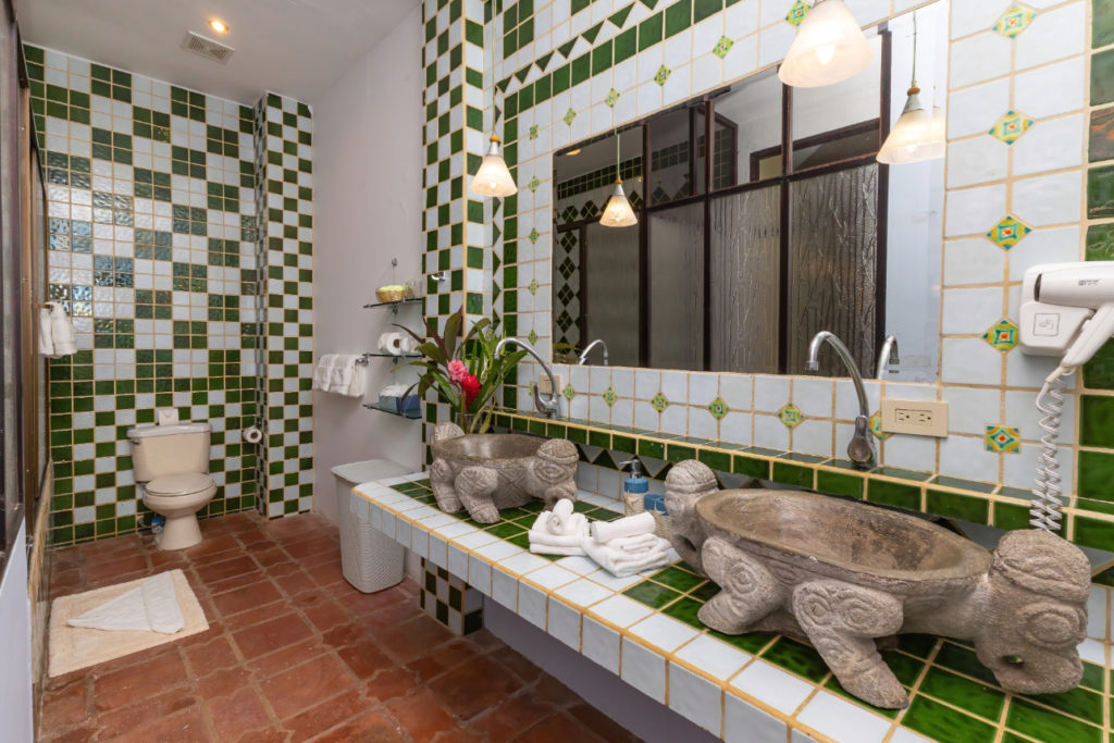 The bathroom showcases a distinctive design with ceramic tiled countertops and a hand-carved stone sink.