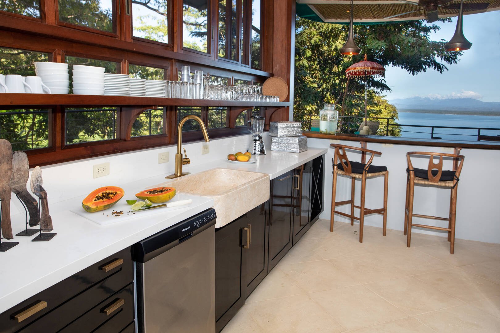 Light-filled kitchen with open shelving, artisan finishes, and a bar overlooking the Pacific Ocean in Manuel Antonio