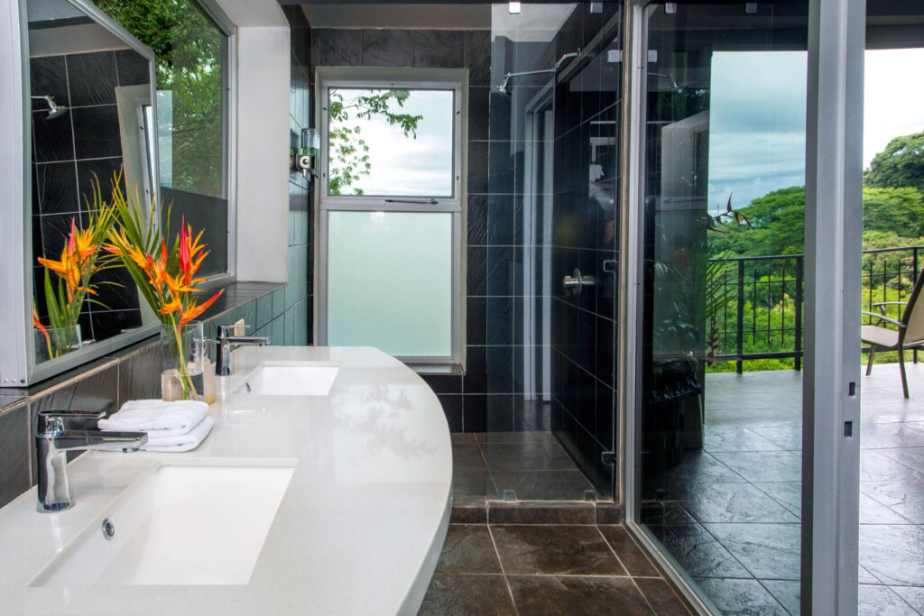 This classy bathroom has dark tile, a cool white stone counter, and an awesome rainforest view.