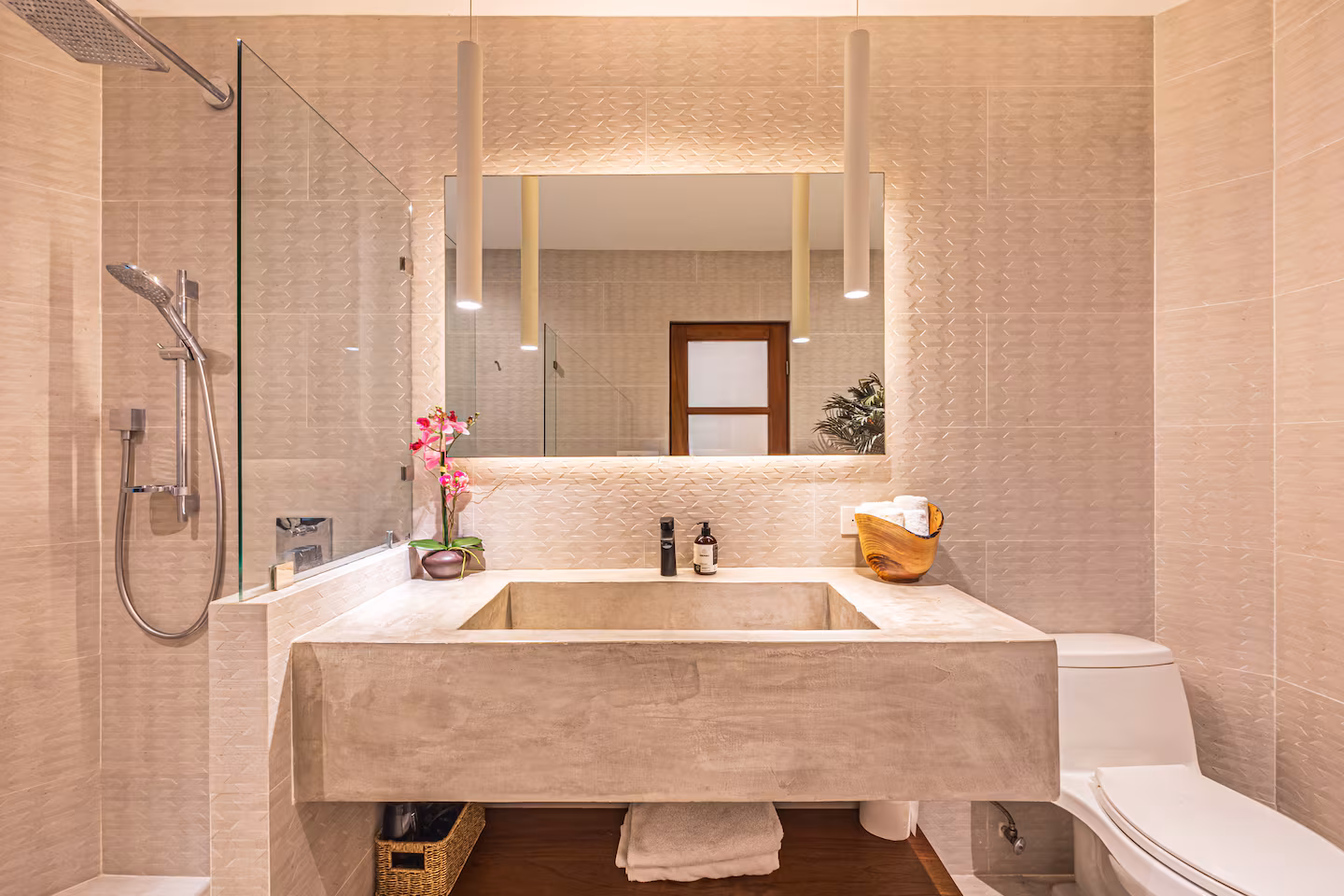 Modern bathroom with concrete vanity, textured tile walls, glass shower, and soft pendant lighting in a villa near Dominical, Costa Rica.