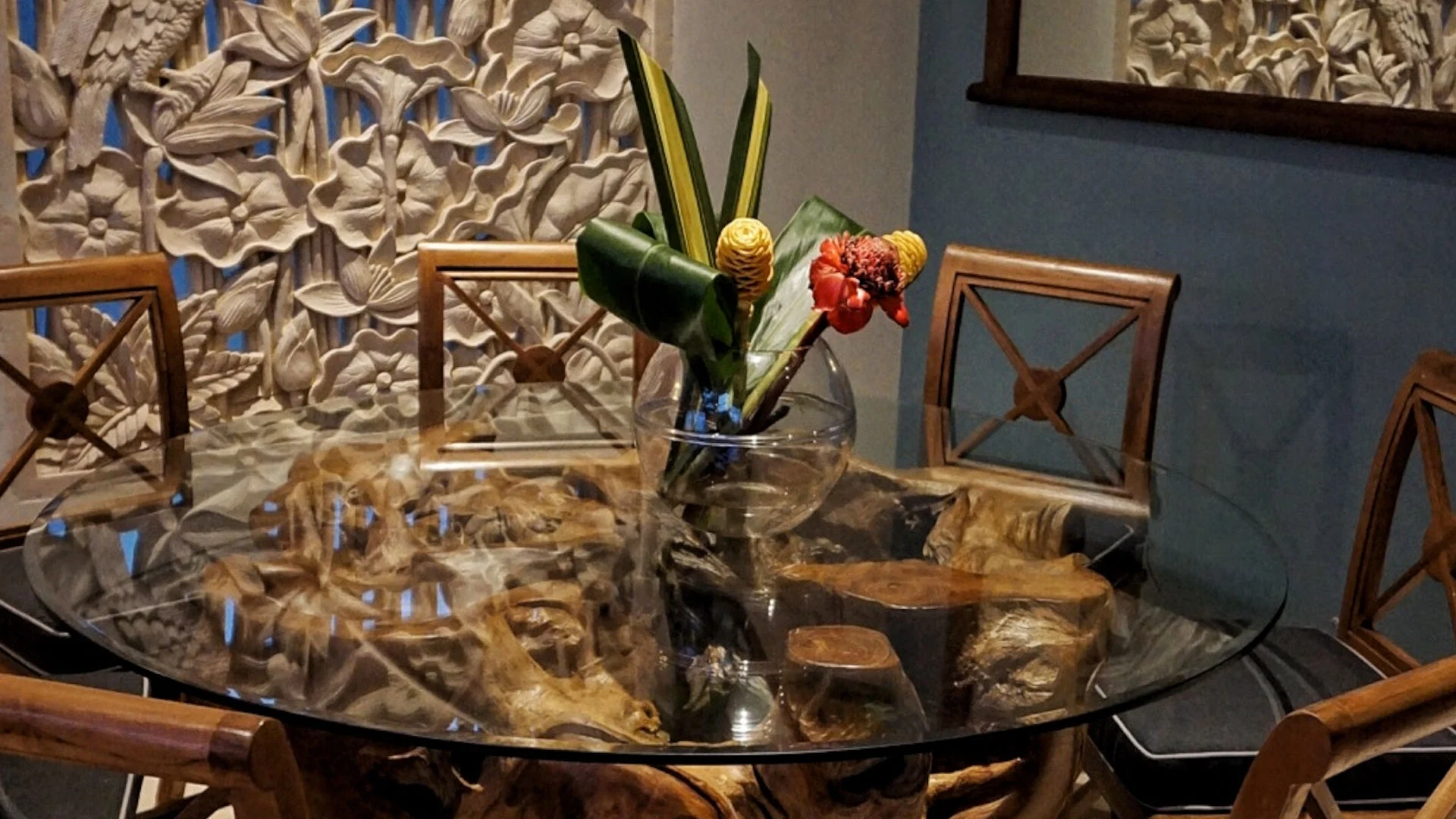 Artisanal dining table with sculpted driftwood base, glass top, and tropical floral centerpiece in Manuel Antonio