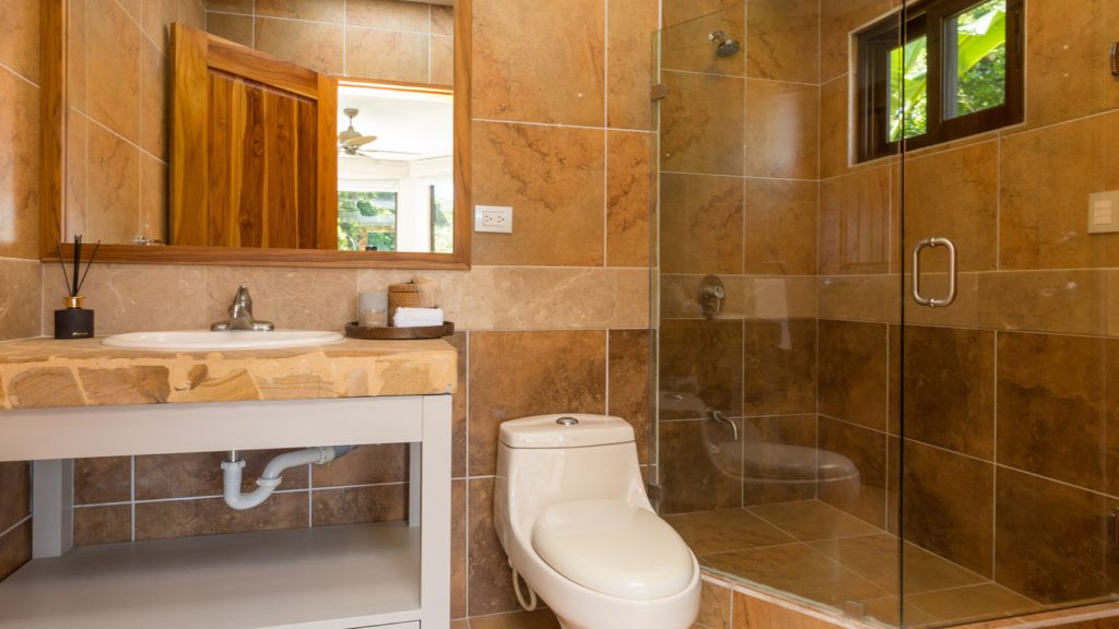 This bathroom has a glass-door shower and is tastefully decorated with beautiful tile and a natural stone counter.