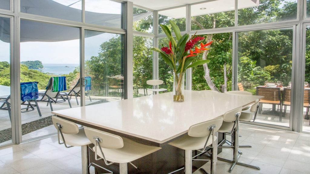 The views from the island dining room through the glass walls are a spectacular combination of the ocean and surrounding tropical rain forest at this vacation home in Manuel Antonio.