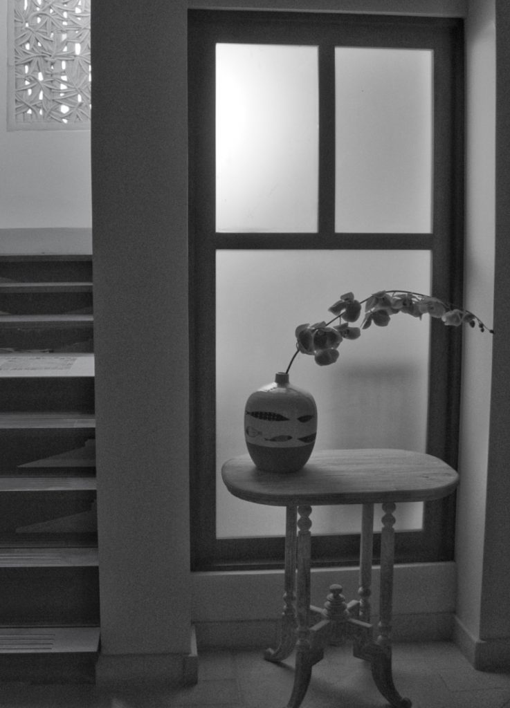 A black and white photo of the stairway and side table. 