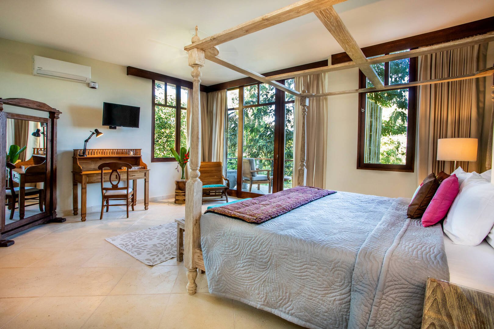 Light-filled master bedroom with rustic canopy bed, writing desk, and terrace views surrounded by greenery in Manuel Antonio