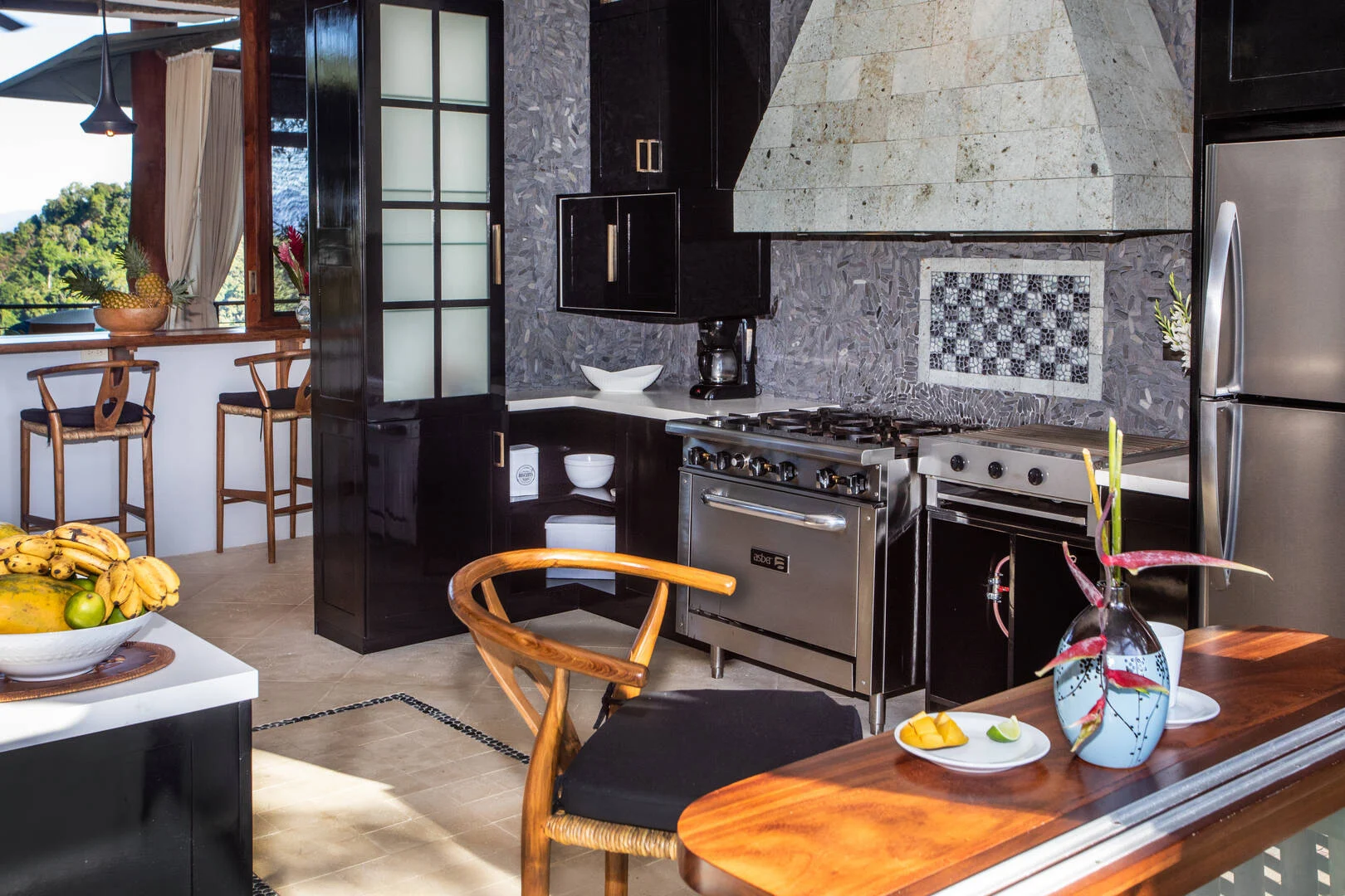 Open kitchen with chef-grade appliances, stone finishes, and bar seating overlooking tropical greenery in Manuel Antonio