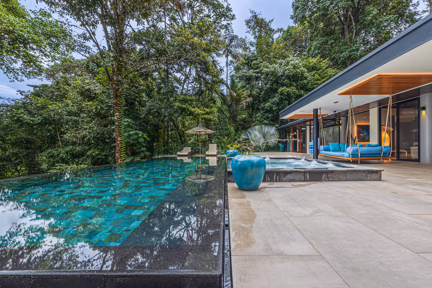Infinity-edge pool surrounded by tropical rainforest with outdoor lounge areas and modern villa architecture near Dominical, Costa Rica.