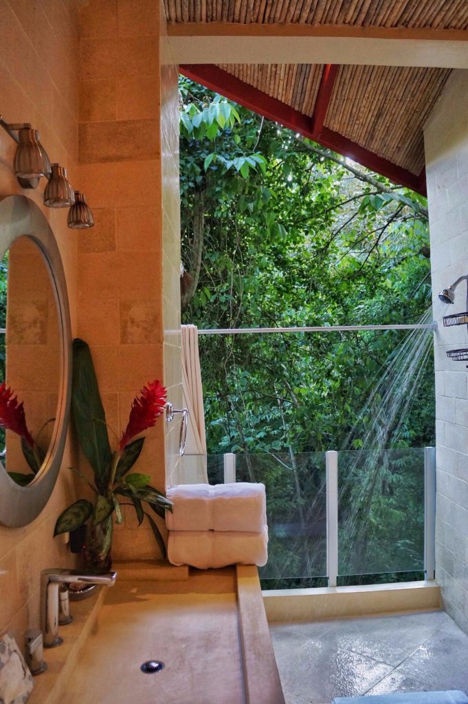 An open-air shower with a jungle view creates a tropical feel in this bathroom with unique stone and tile accents.