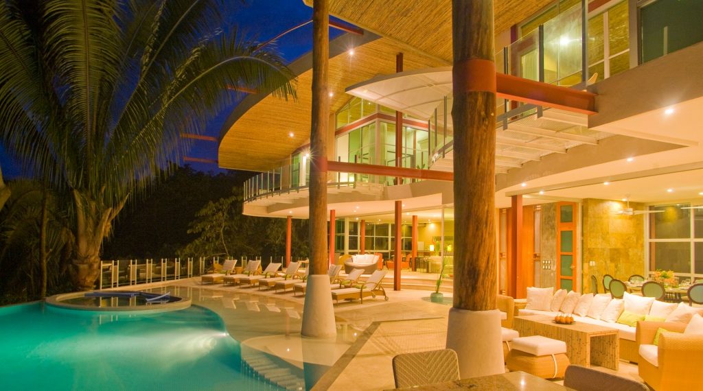 Custom lighting creates a warm glow over the beautiful pool, deck, and main salon at night.