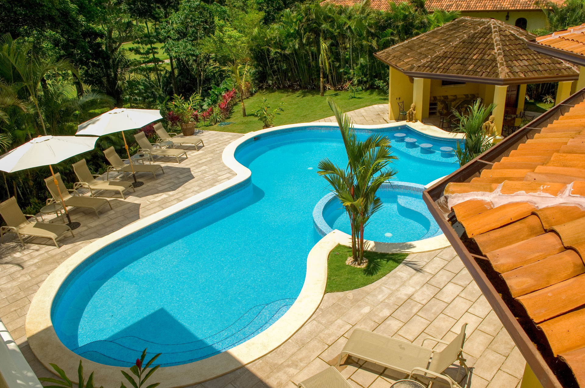 Elevated view of curved private pool, jacuzzi, and shaded poolside pavilion.
