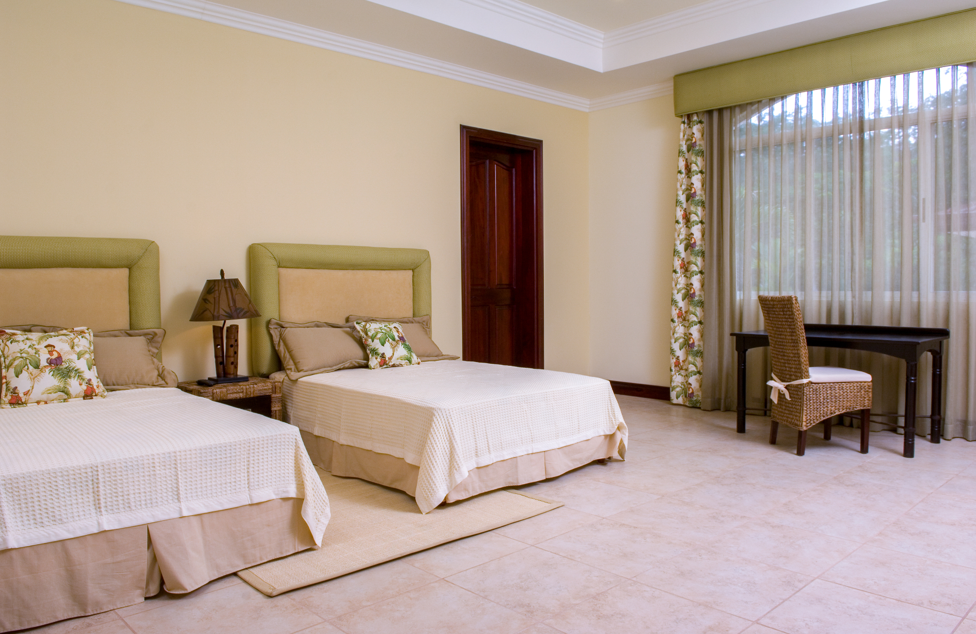 Bedroom with two beds and desk beside a large window.