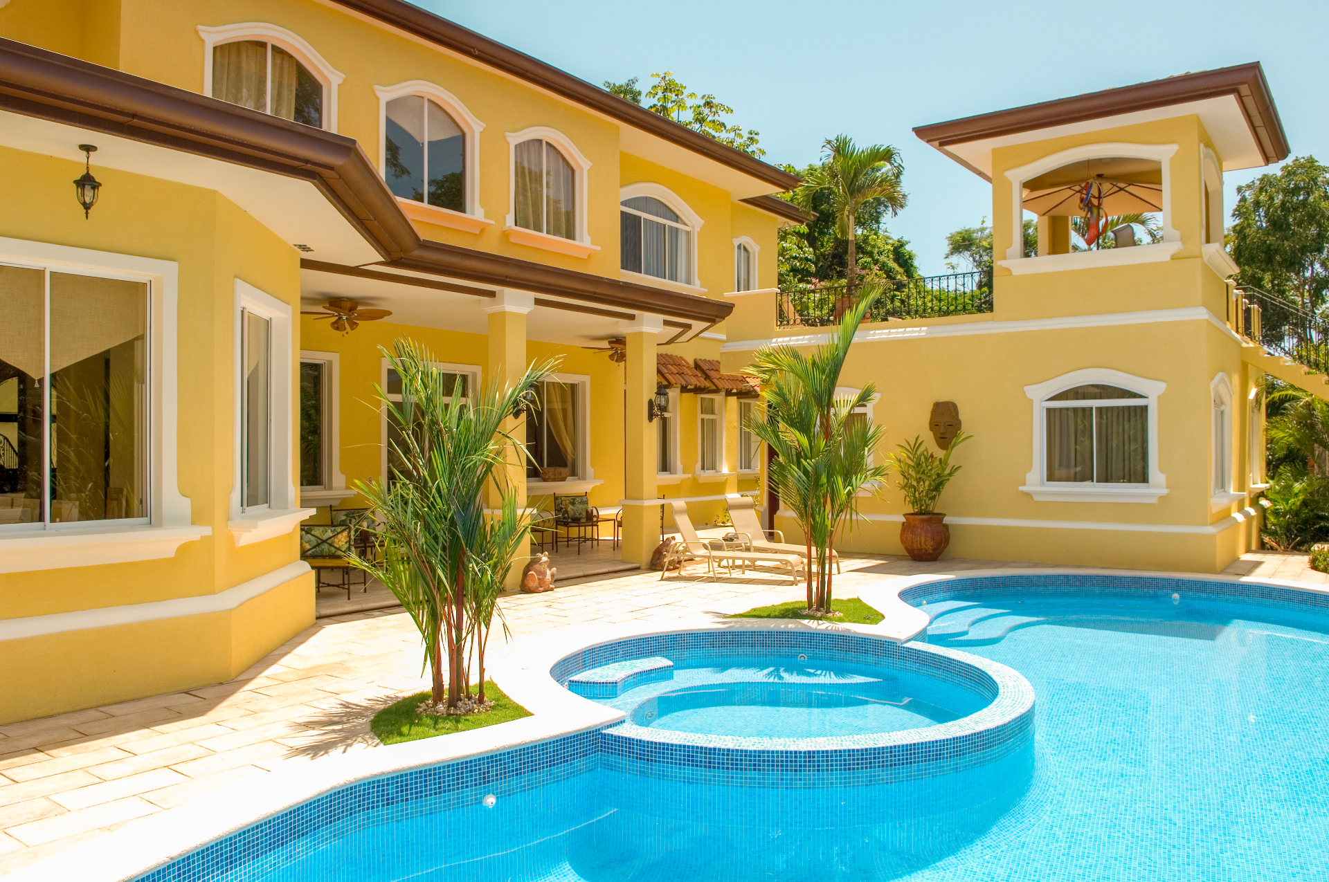 Sunlit villa pool terrace with jacuzzi and shaded outdoor seating beside the main house.