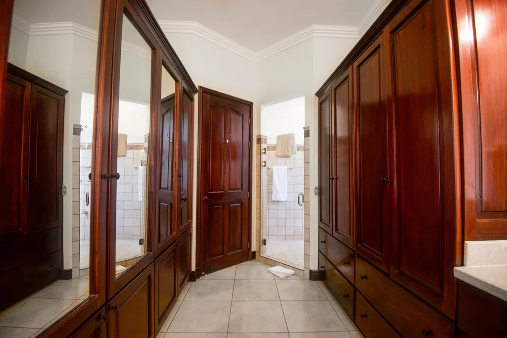 A spacious walk-in closet with custom wood cabinetry leads toward the villa’s ensuite bathroom and shower.