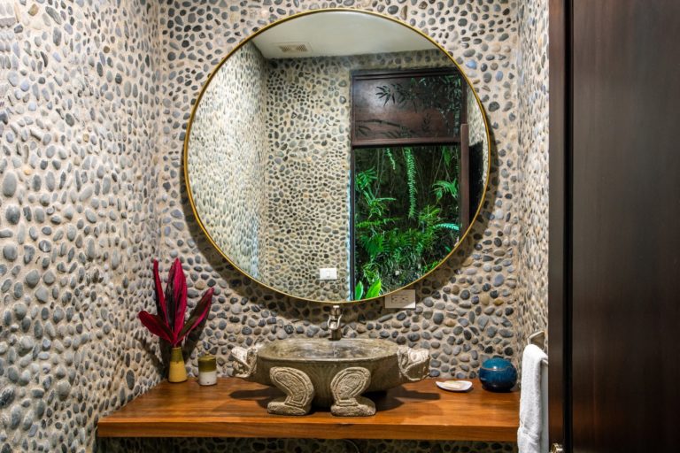 Powder room with stone walls, round mirror, and carved stone sink in Manuel Antonio Costa Rica