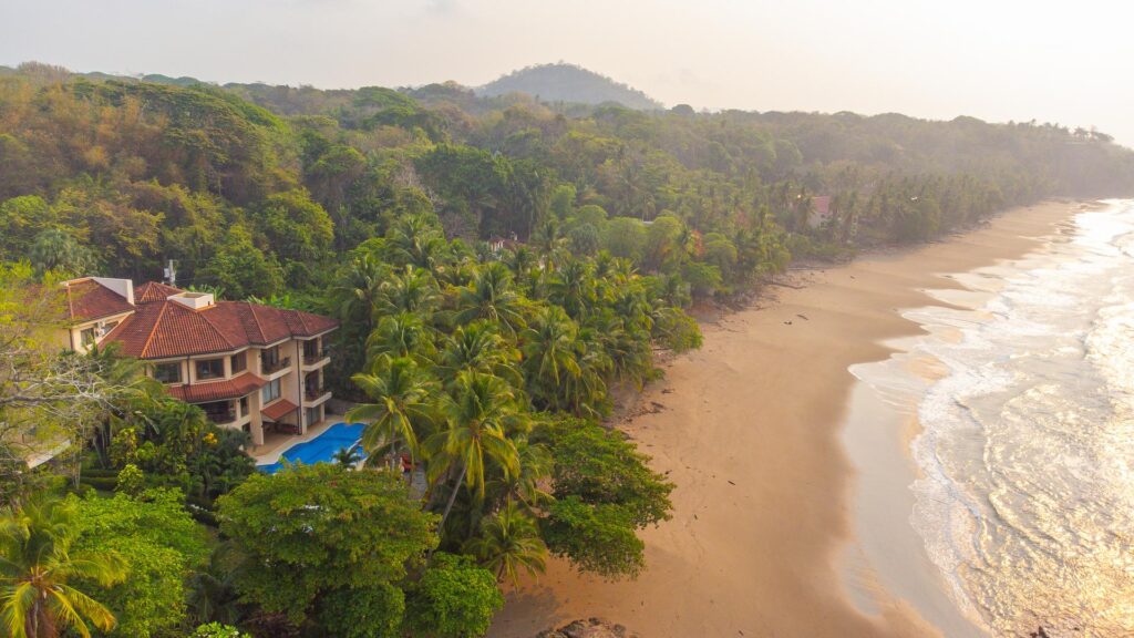 Aerial view of a luxury beachfront estate on Playa Tambor, Costa Rica, surrounded by tropical rainforest and the Pacific Ocean.