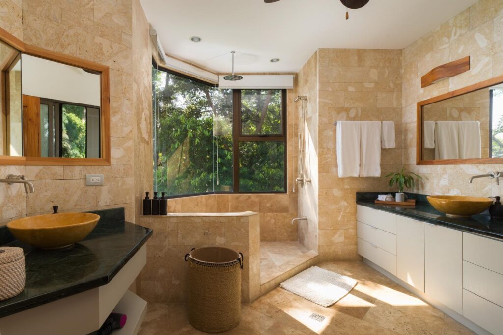 A soothing, spa-inspired bathroom featuring rich stone finishes, dual vanities, and tranquil rainforest views that create a naturally calming retreat.