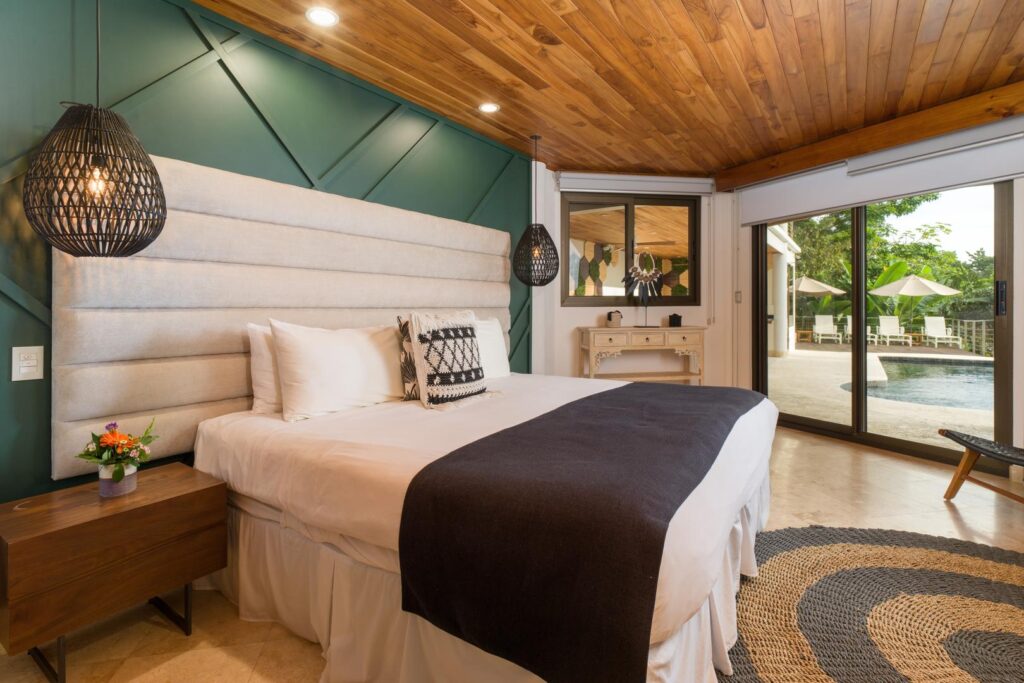 A stylish poolside bedroom featuring modern décor, rich wood ceilings, and sliding doors that open straight onto the bright terrace and inviting pool.