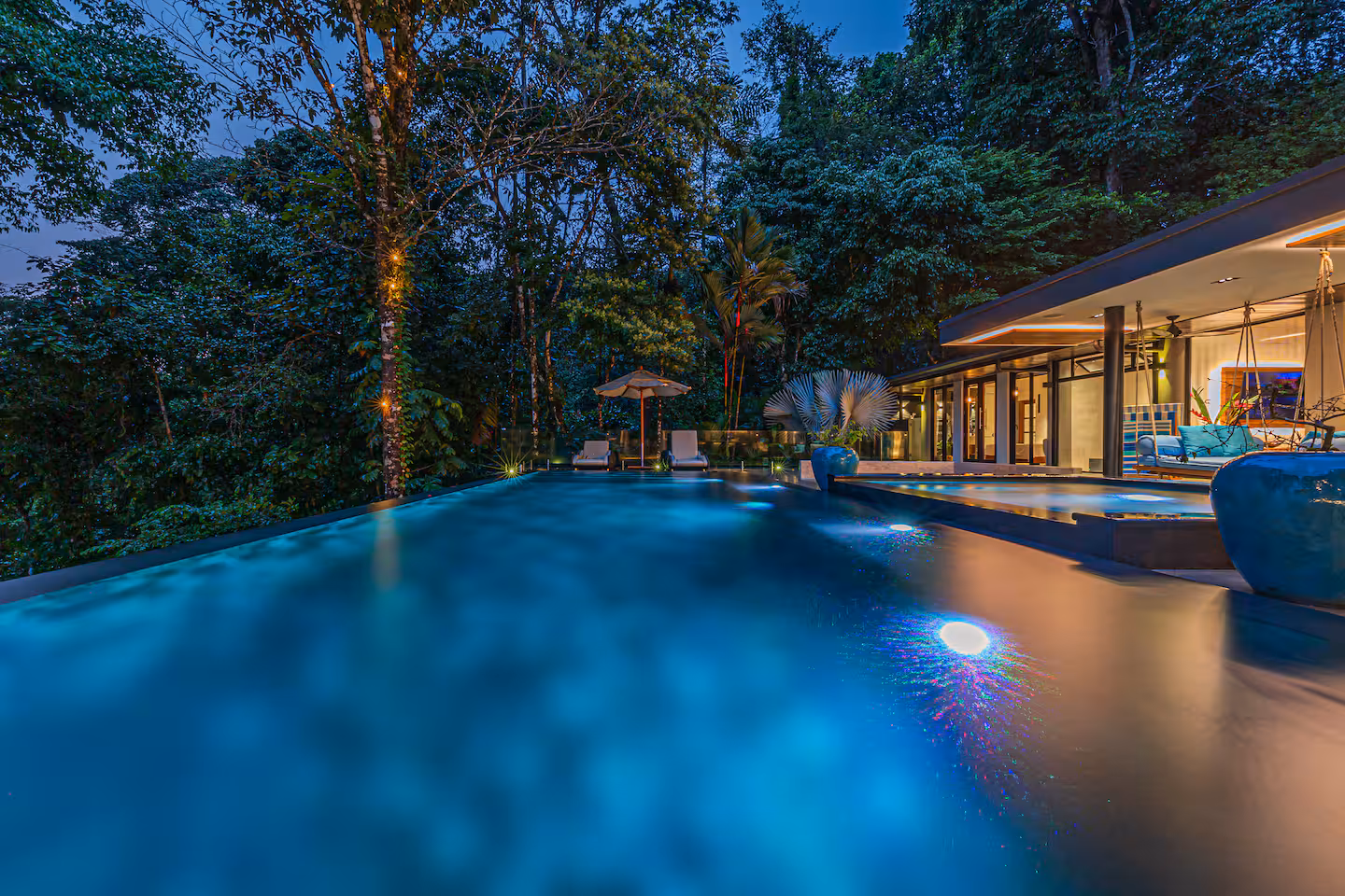 Infinity pool illuminated at night with jungle surroundings and modern villa lighting near Dominical, Costa Rica.