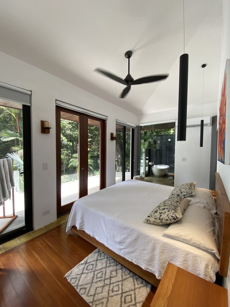 The master bedroom has doors to open, blinds to close, and is surrounded by lush green foliage.