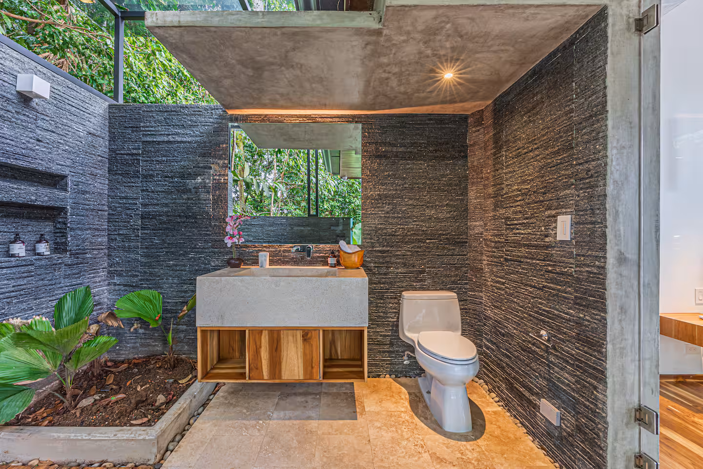 Open-air bathroom with vanity, toilet, large windows, and garden views in a luxury villa near Dominical, Costa Rica.