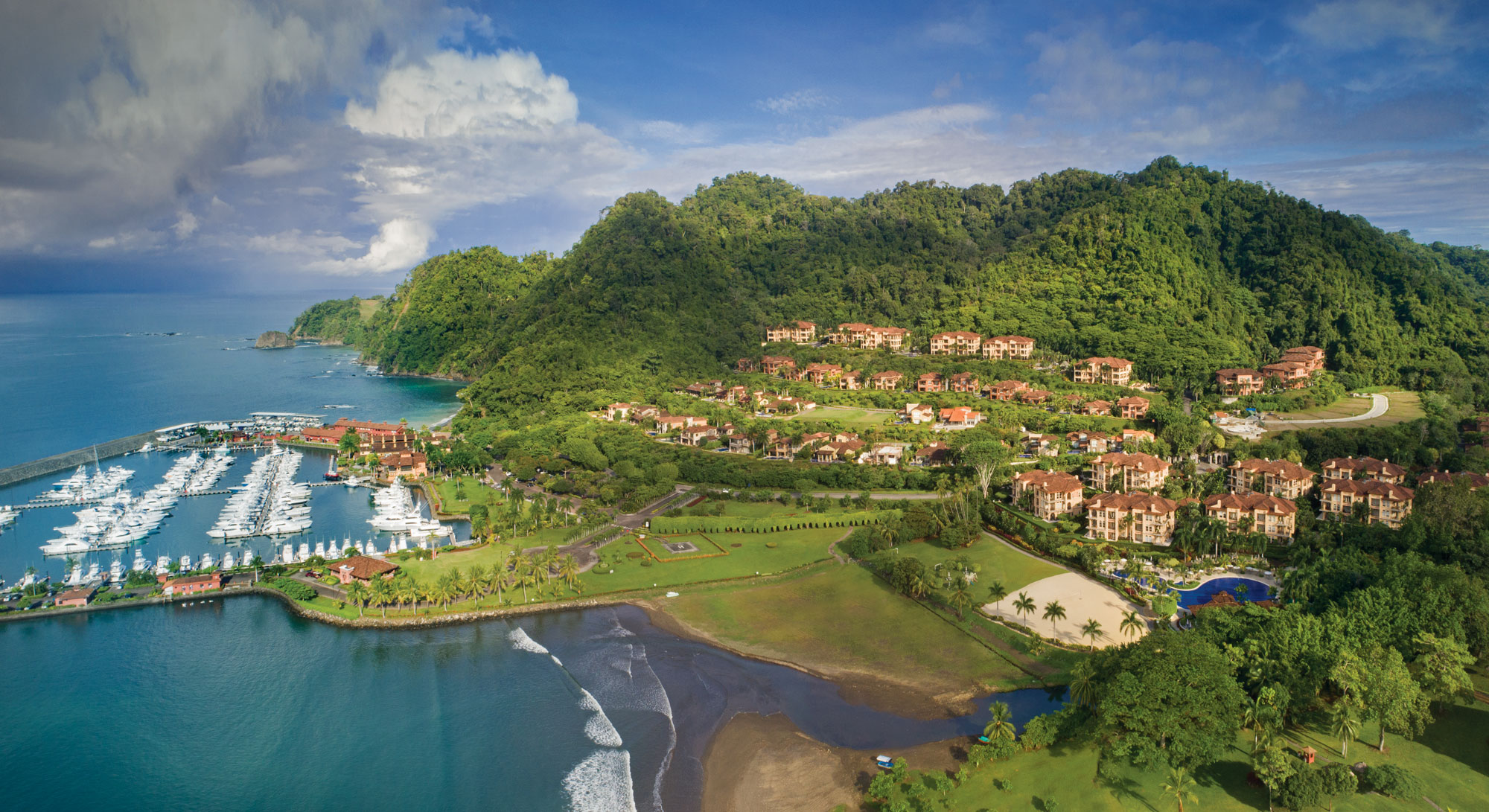 Aerial view of Los Sueños Resort and Marina with yachts, coastline, and surrounding tropical hills.