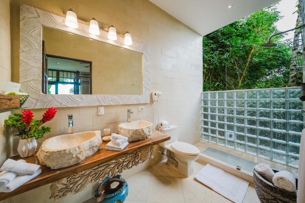 Indulge in a spa-like experience with an open-air shower surrounded by lush greenery and handcrafted natural stone finishes.