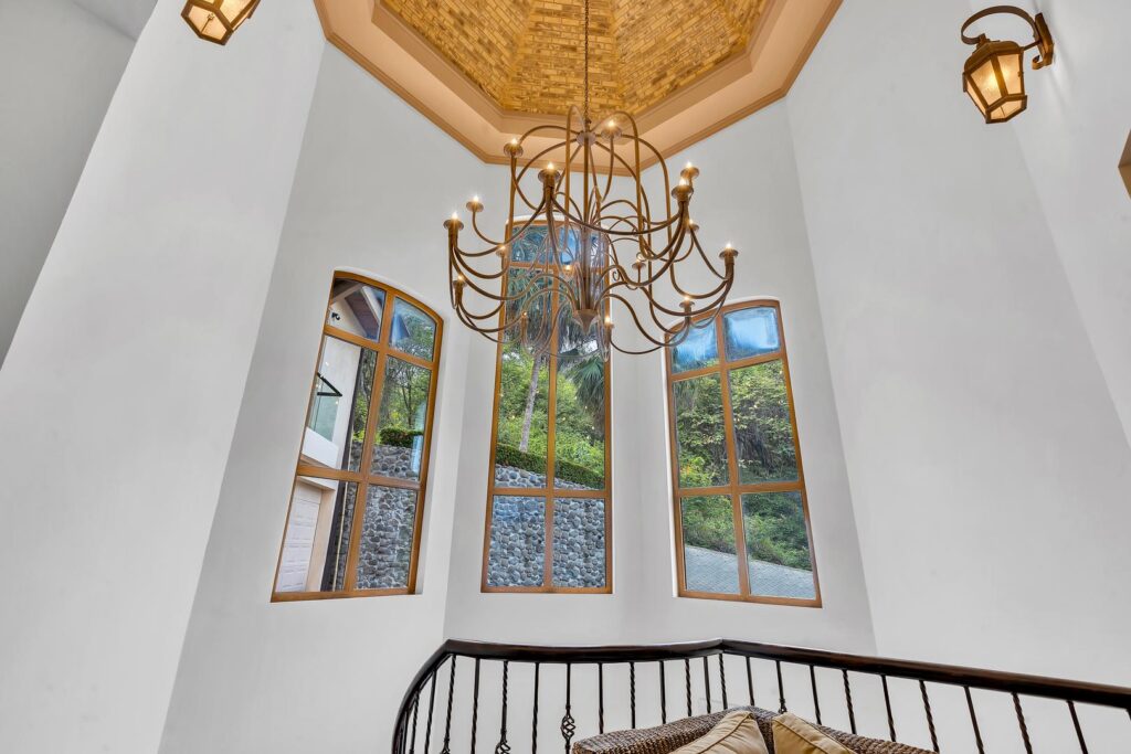 Golden light fills the room through tall windows, highlighting the chandelier above the staircase.