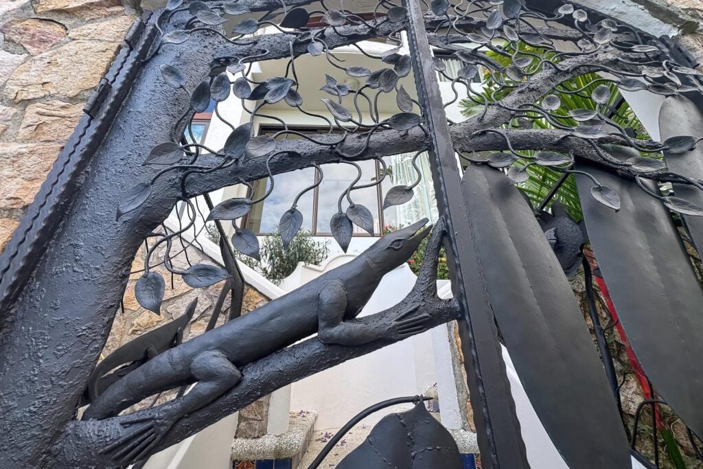 A custom iron gate marks the entrance to the villa, where artistic craftsmanship and nature-inspired details offer a striking first impression.