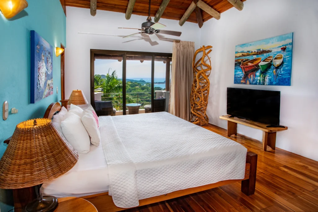 A serene ocean-view bedroom where warm wood details, soft light, and sliding doors open to a private terrace overlooking the Pacific.