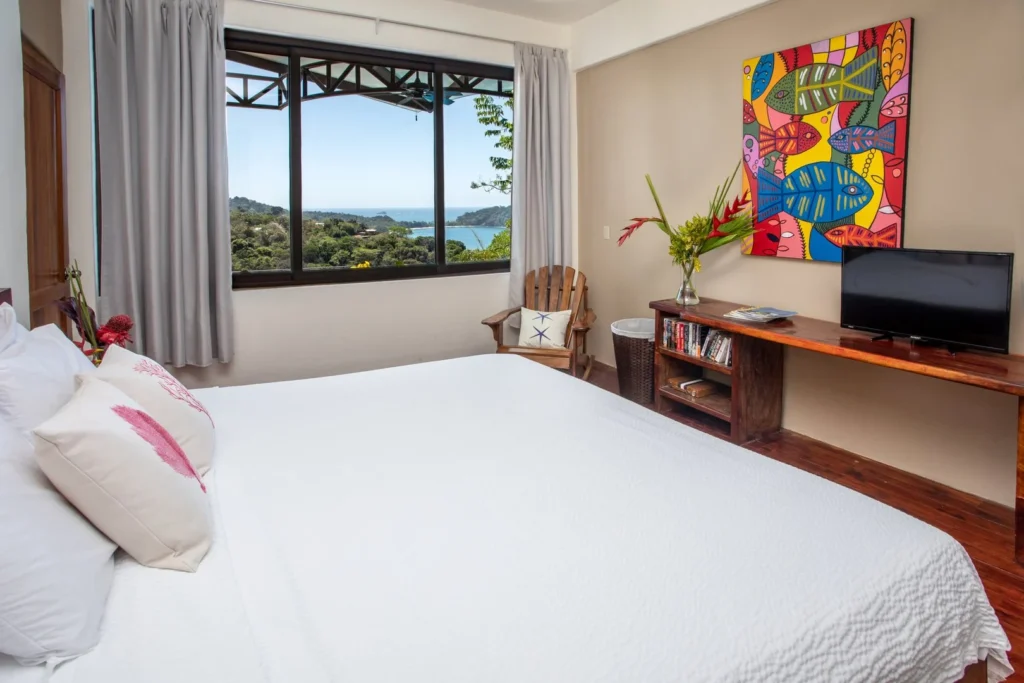 A bright bedroom framed by large windows, where natural light and distant ocean views create a calm, inviting space to relax and recharge.