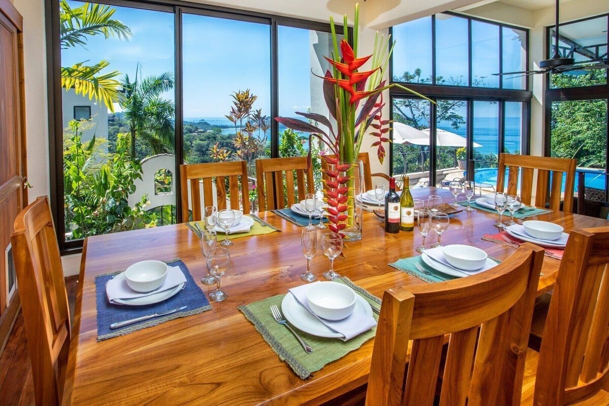 Wooden dining table set for a group with ocean and jungle views through large glass windows