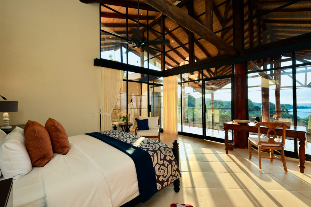 The master suite showcases ingeniously designed tall ceilings with a captivating natural wood framework, and tall glass doors present sublime vistas of Manuel Antonio National Park.