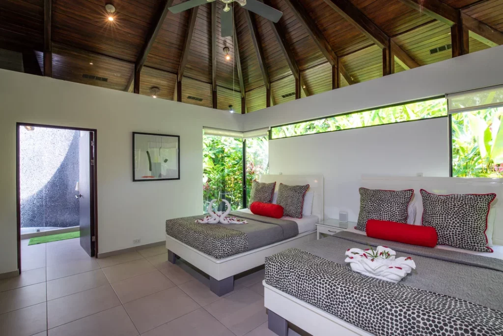 This bedroom is adorned with two queen beds and an open patio boasting views of exotic gardens.