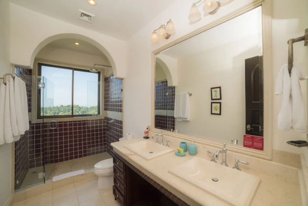 This bathroom includes dual sinks on a granite countertop and a spacious shower with ocean views.