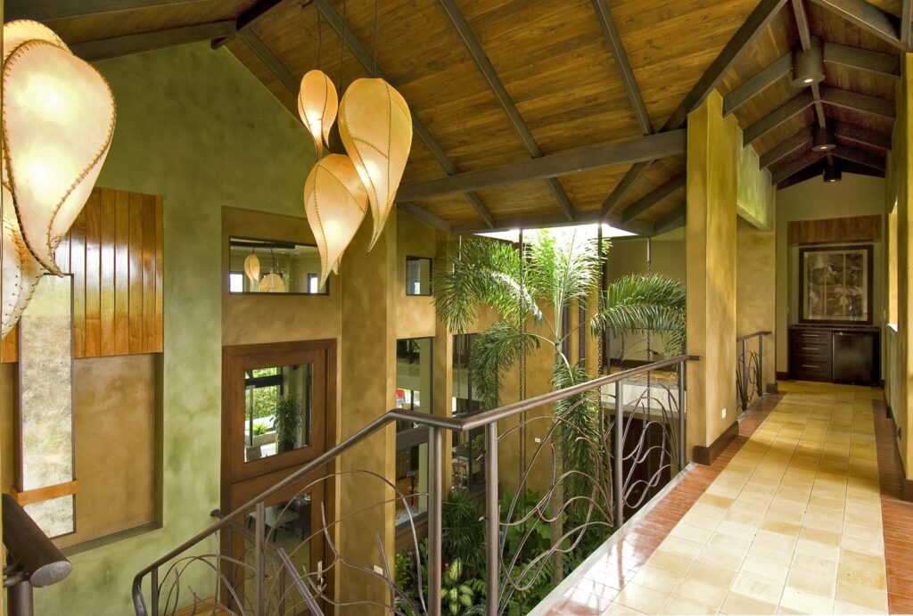 Open corridor floating above greenery with natural light and handcrafted pendants.
