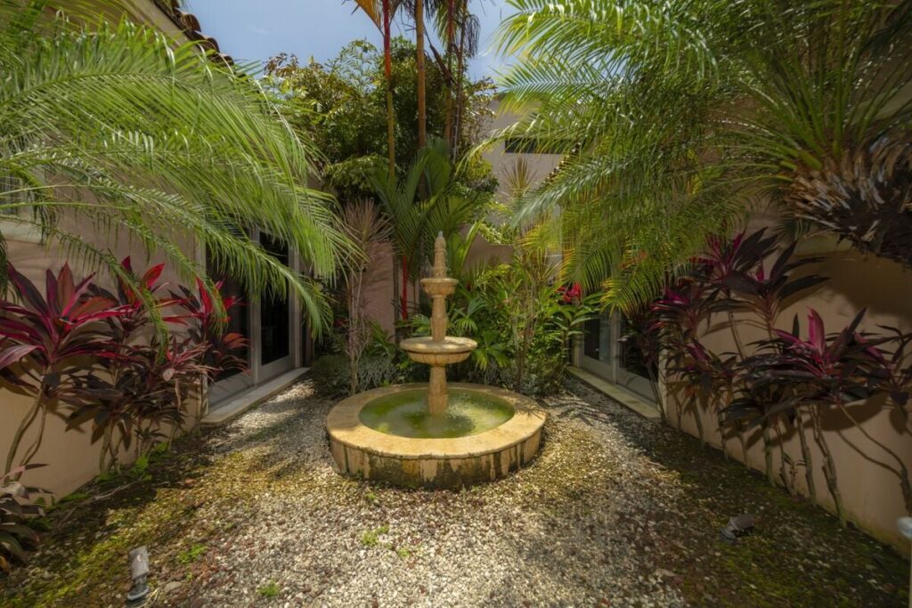 A private tropical courtyard with a central fountain creates a peaceful retreat, blending lush greenery with tranquil water features.