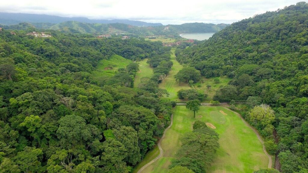 An aerial view of Los Sueños showcasing the golf course set within lush rainforest, with the Pacific coastline visible in the distance.