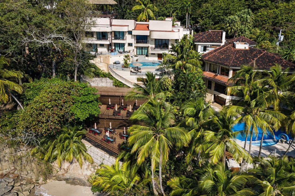 Aerial view of a luxury beachfront villa showcasing tropical gardens, multiple outdoor living spaces, and direct access to a secluded Pacific beach.