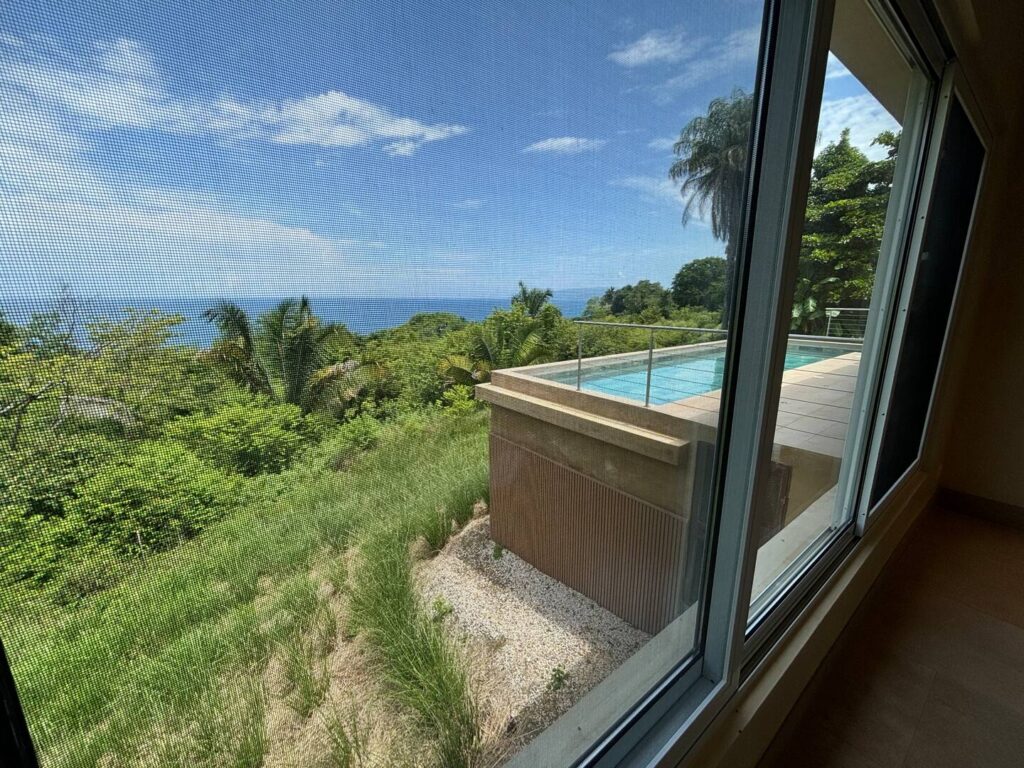 Views from the bedroom overlook the private pool, lush tropical forest, and the Pacific Ocean beyond.
